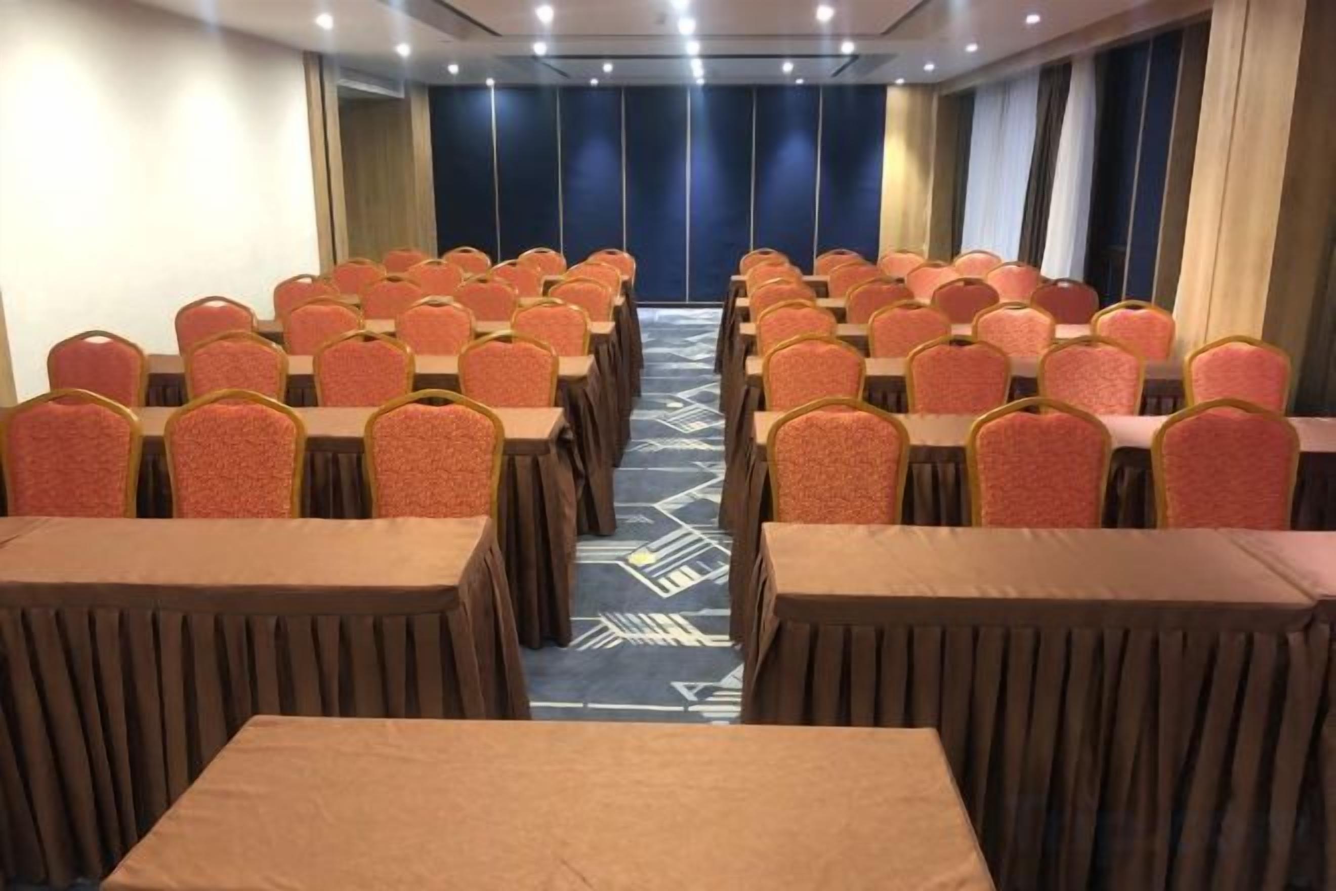 Ein Konferenzraum mit Tischen und Stühlen, einem gemusterten Teppich und Blick auf eine blaue Glasfassade.