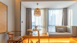 Una habitación de hotel moderna con un sofá, una silla de madera, una mesita y una lámpara colgante.
