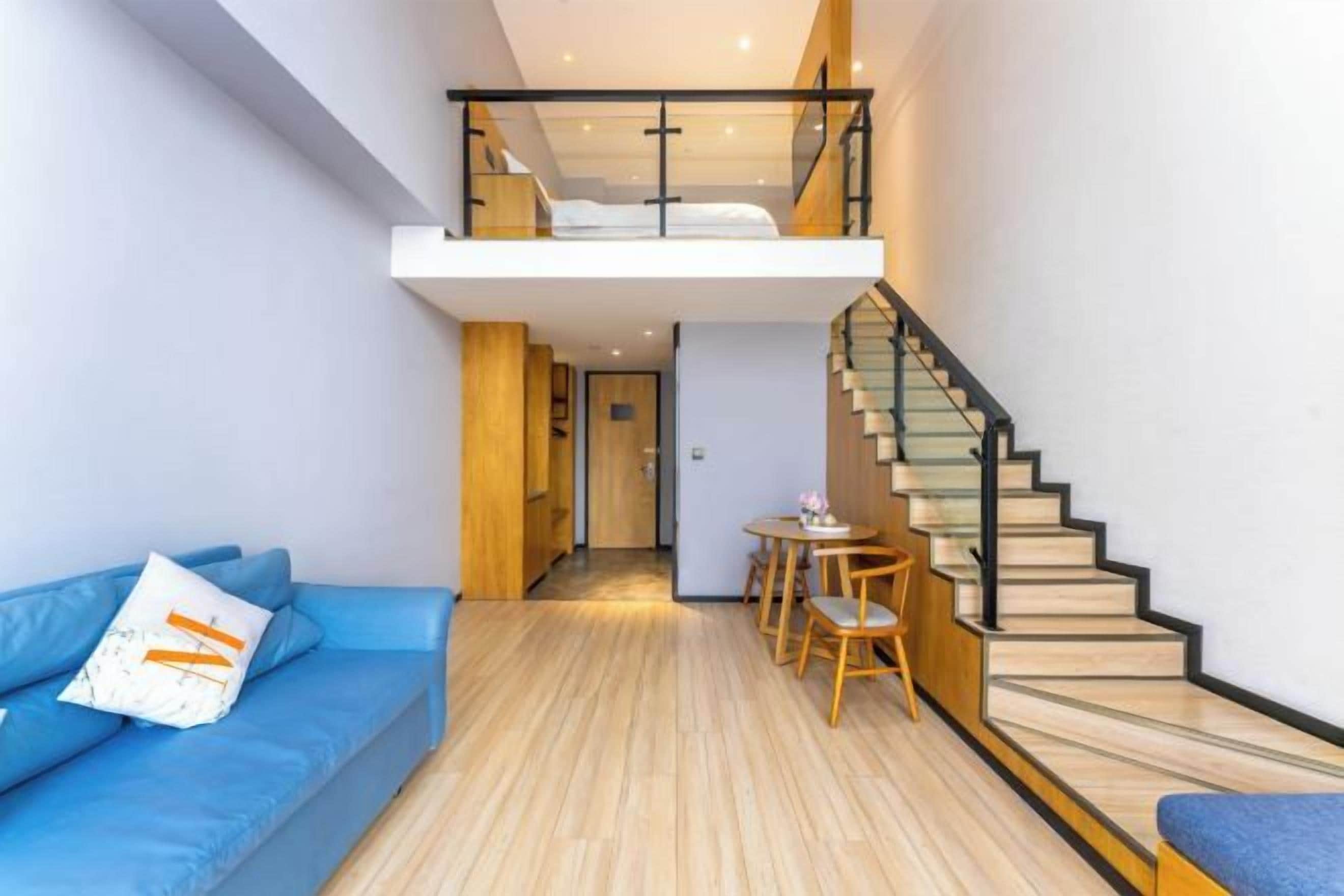 A modern interior with a loft bedroom, a staircase, a dining area, and a blue sofa.