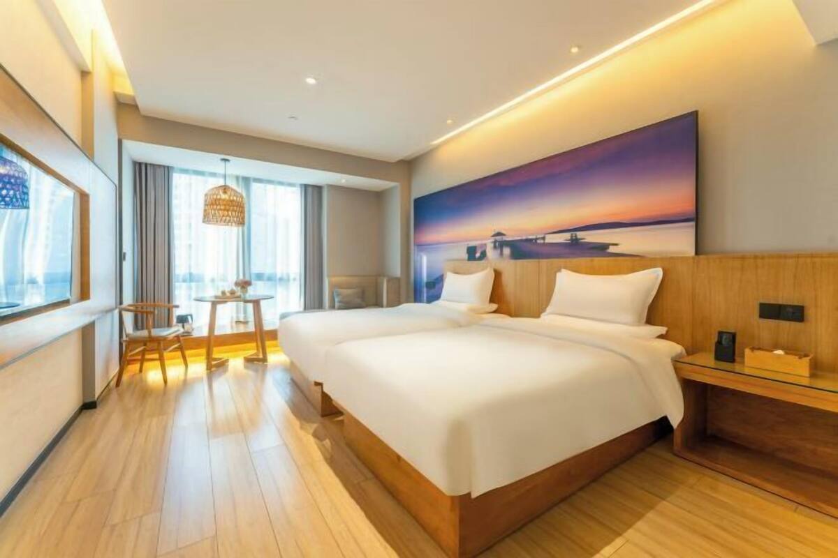 A modern hotel room with a large bed, a small table, a chair, and a painting on the wall.