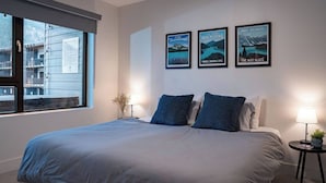 Habitación de hotel moderna con una cama grande, una ventana con vistas a edificios y tres carteles enmarcados en la pared.