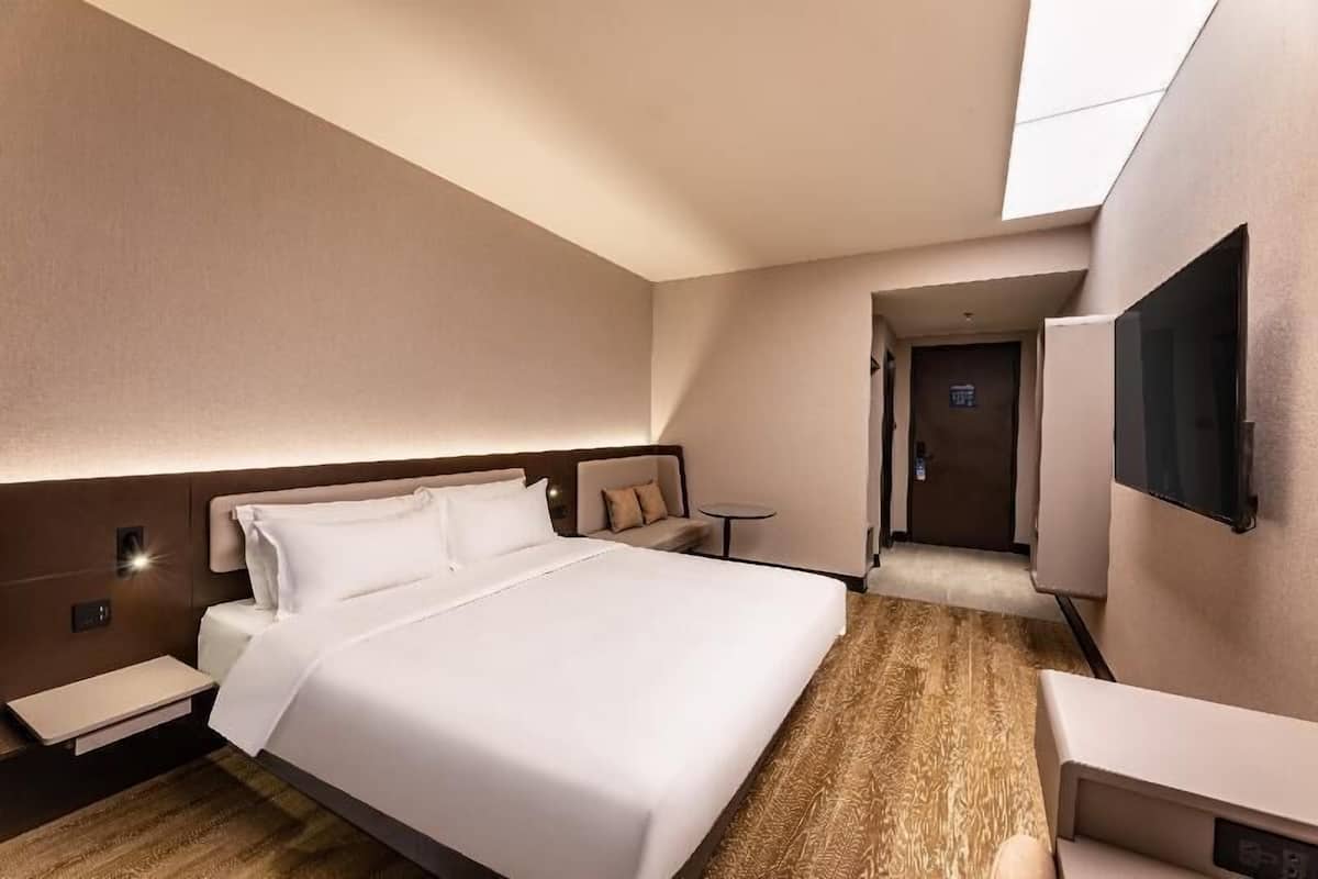 A modern hotel room with a large bed, bedside tables, a desk, and a TV mounted on the wall.