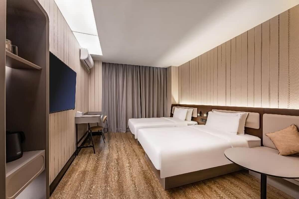 A hotel room with two beds, a desk, a chair, a small table, and a wardrobe.