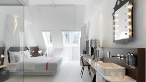 Ein modernes Hotelzimmer mit Bett, Nachttisch, Schminktisch mit Spiegel und einem Badezimmer mit Badewanne.