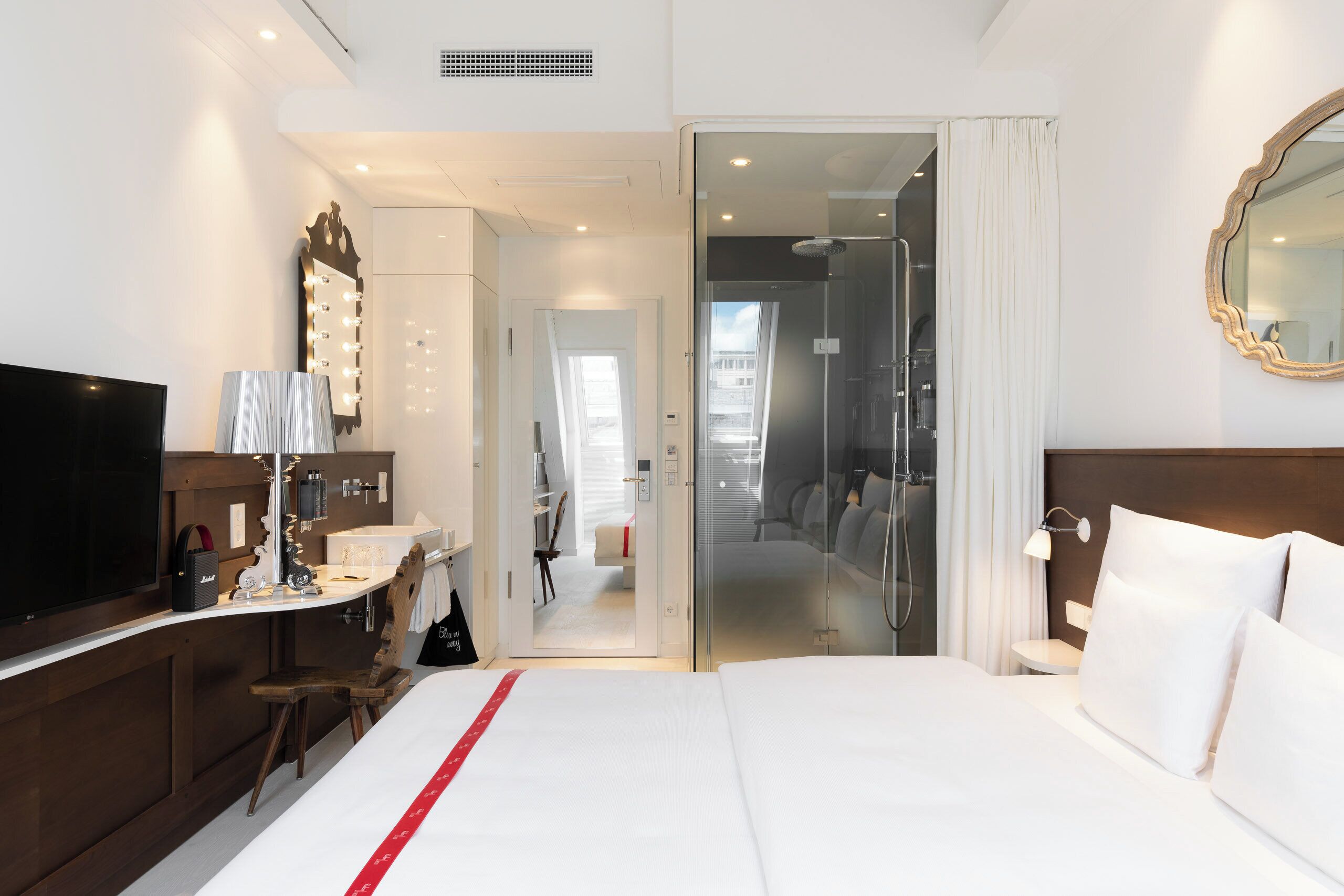 Une chambre d’hôtel avec un lit, une coiffeuse avec un miroir, une télévision et une salle de bain visible à travers une porte ouverte.