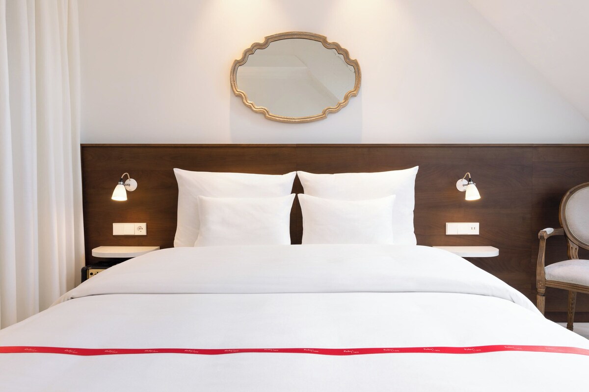 A hotel room with a large bed, two bedside tables, a mirror, and a chair.