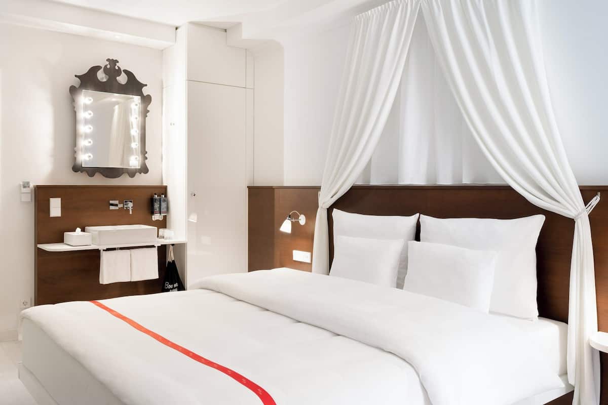A hotel room with a bed, a vanity with a mirror, and a nightstand.