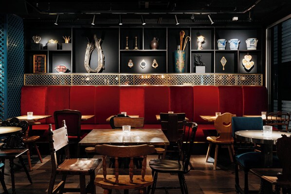 A restaurant interior with red booths, wooden tables, and a variety of displayed items on shelves. - Ruby Rosi Hotel Munich by IHG (Munich)