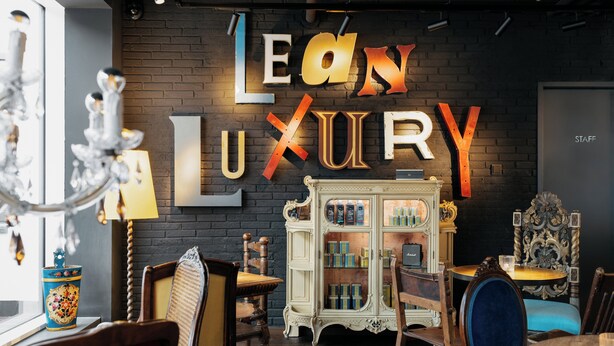 Ein Hotel im Boutique-Stil mit Backsteinwand, einem großen 'LEON LUXURY'-Schild, antiken Möbeln und einem Vintage-Schrank mit Glastüren.