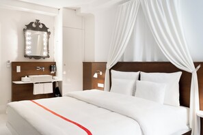 A hotel room with a bed, a vanity with a mirror, and a nightstand. - Ruby Rosi Hotel Munich by IHG (Munich)