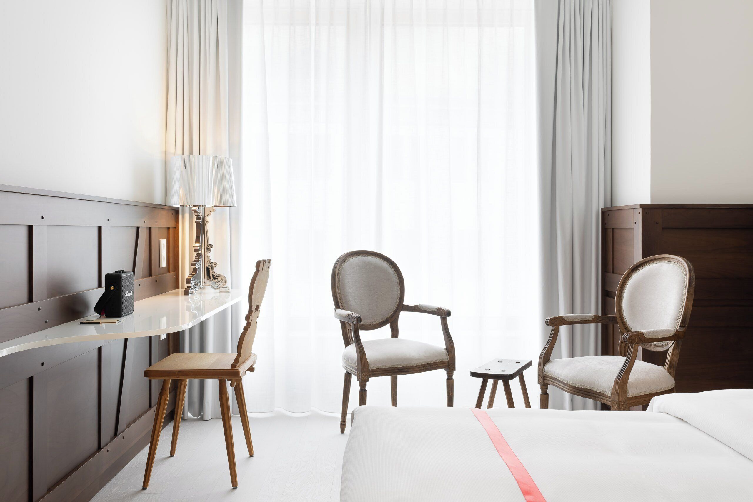 A hotel room with a bed, two chairs, a desk with a lamp, and a small table.