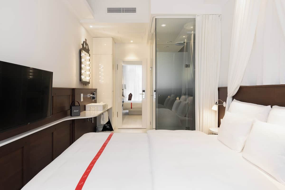 A hotel room with a large bed, a television, a vanity with a mirror, and a walk-in closet.