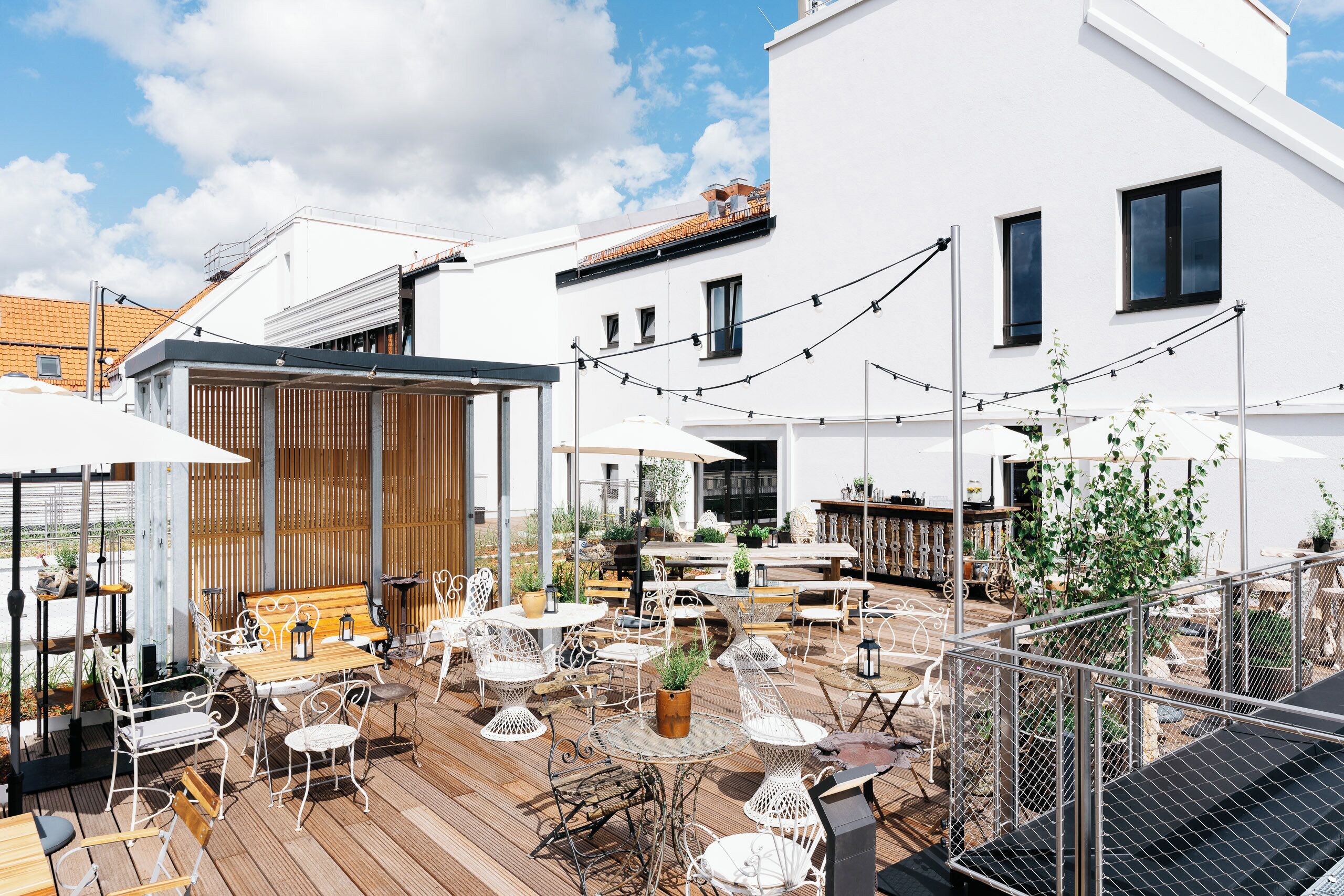 An outdoor patio with tables and chairs, a wooden deck, and a white building in the background.