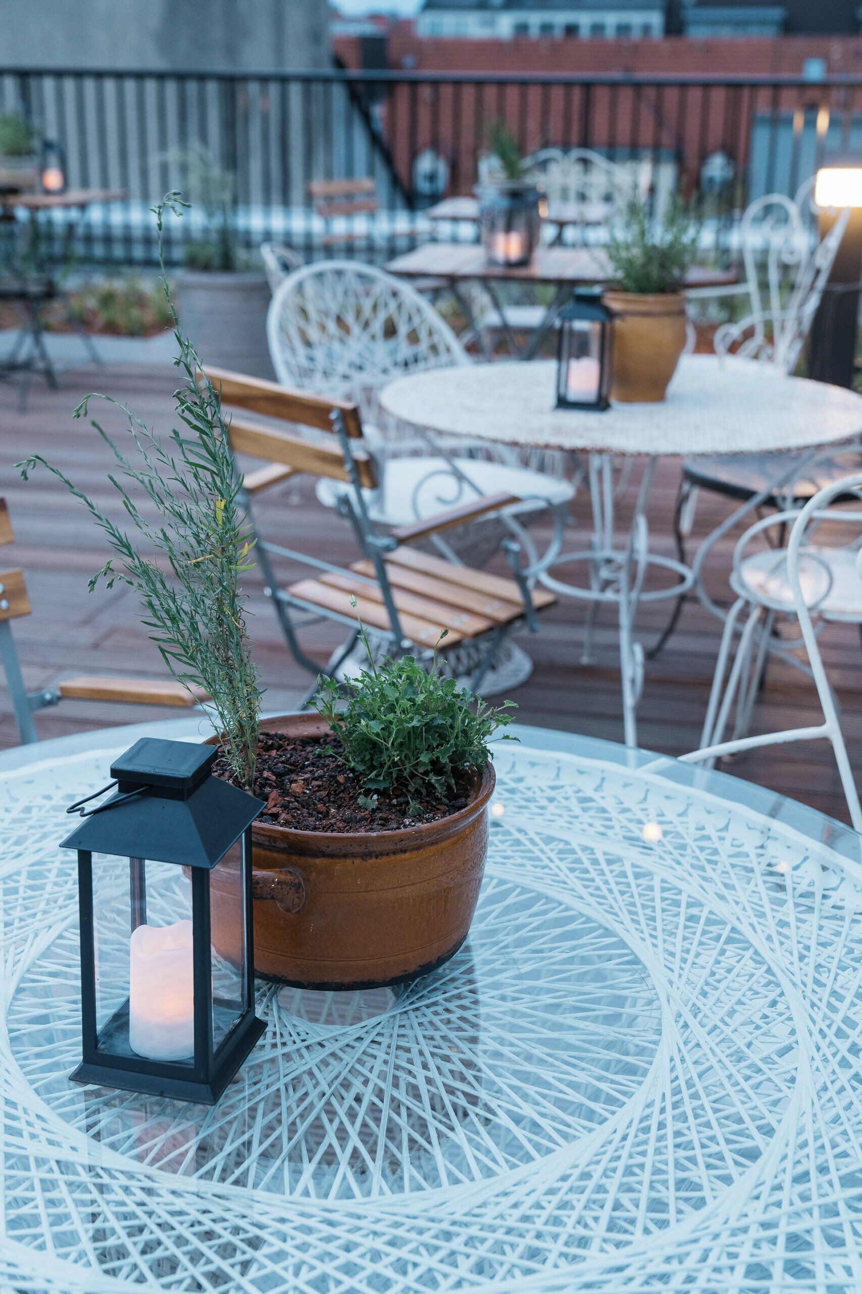 An outdoor patio with round tables and chairs, potted plants, and a lantern.