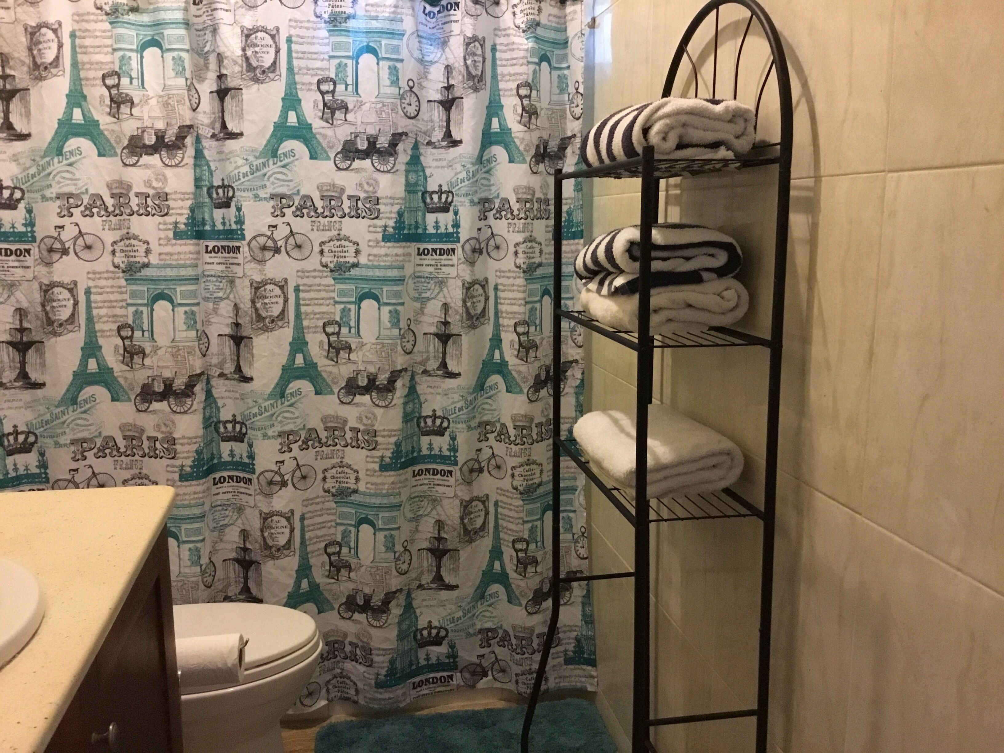A bathroom with a shower curtain featuring Paris and London landmarks, a toilet, a sink, and a towel rack with folded towels.
