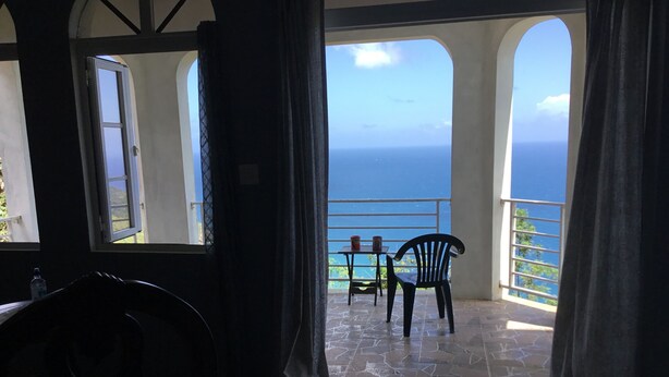 A room with a view of the ocean, a table with chairs, and a bench.