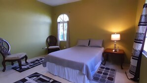 A bedroom with a bed, a chair, a nightstand, a lamp, a window, and a rug.