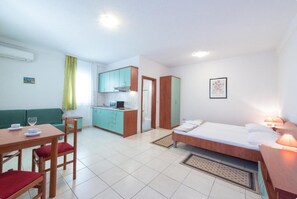 A compact hotel room with a bed, a small kitchenette, a dining area with a table and chairs, and a green sofa. - Villa Borna Apartments - Deluxe Studio Apartment - br. 1 (Dubrovnik)