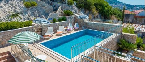 A rooftop swimming pool with stone walls, lounge chairs, and umbrellas.