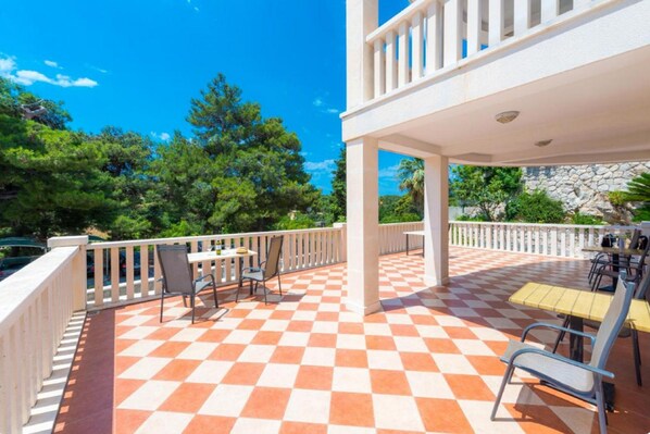 A covered outdoor area with checkered flooring, outdoor seating, and a view of trees and a stone wall.