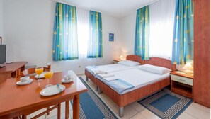 A hotel room with a bed, bedside tables, a desk with a chair, and a dining table set for breakfast.