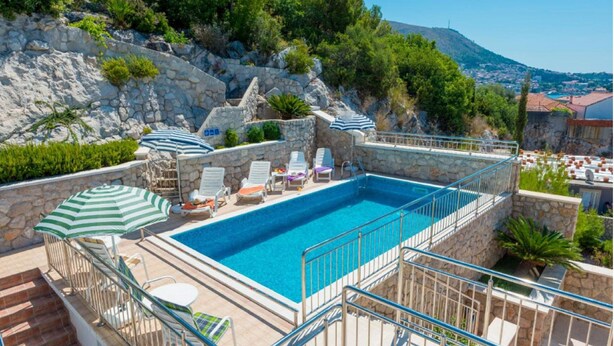 A rooftop swimming pool with stone walls, lounge chairs, and umbrellas.