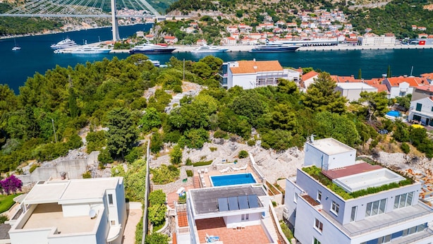 Un pueblo costero con edificios modernos, un puerto deportivo con yates y un puente atirantado al fondo.