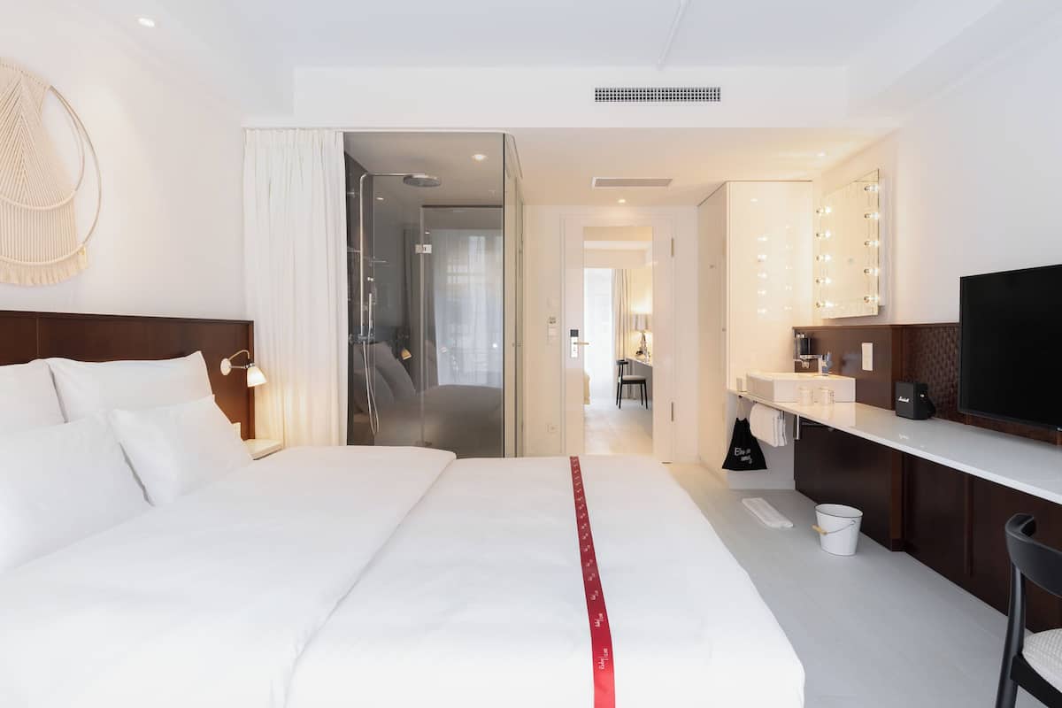 Une chambre d’hôtel comprenant un lit, un bureau, une télévision, une salle de bain avec un miroir et un couloir menant à une autre chambre.