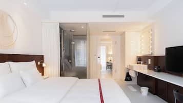 A hotel room with a bed, a desk, a television, a bathroom with a mirror, and a hallway leading to another room.