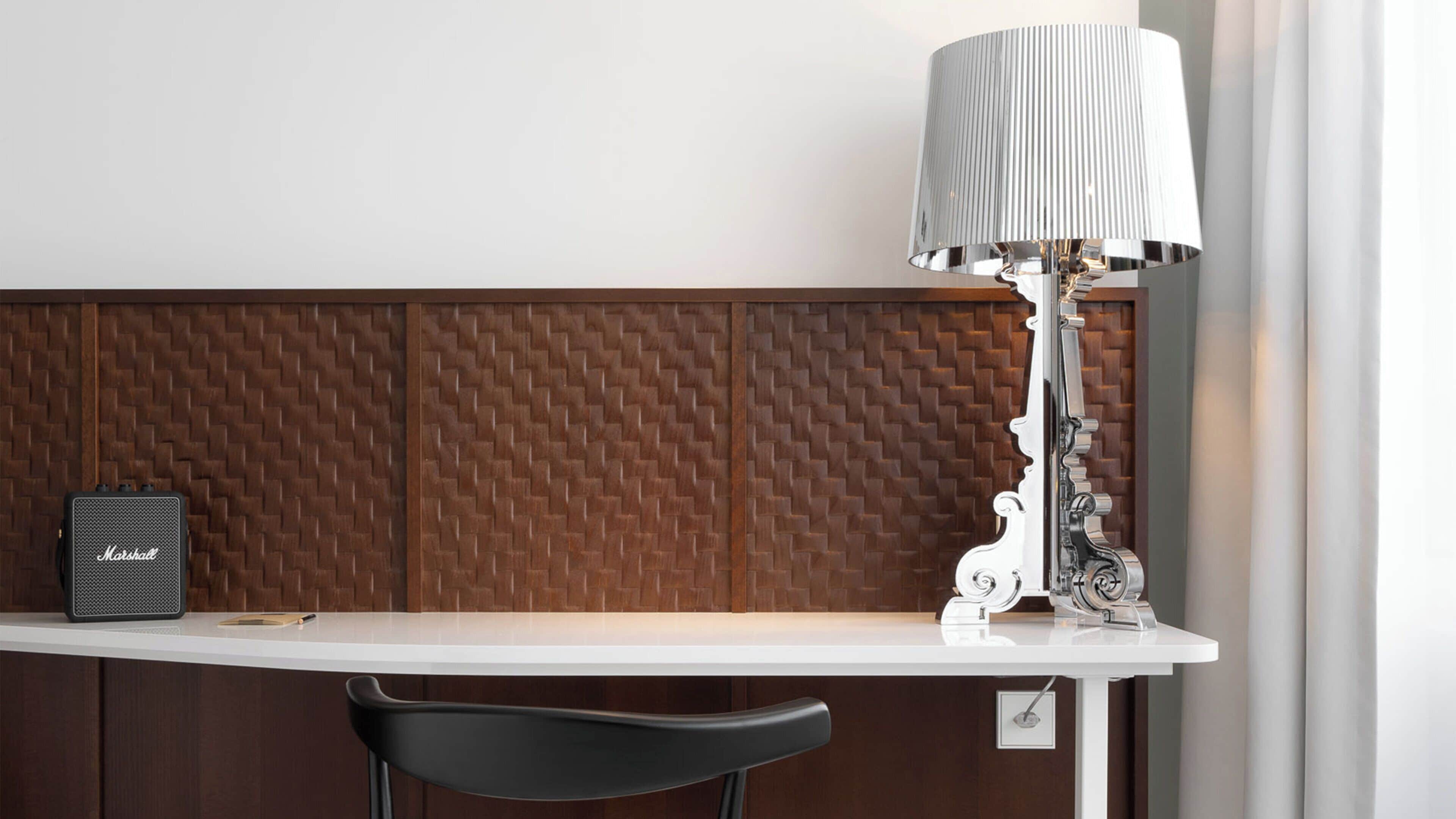 Una mesa blanca con un altavoz negro y una lámpara blanca de pantalla rayada.