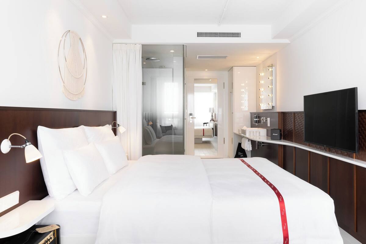 Une chambre d’hôtel avec un grand lit, une coiffeuse avec éclairage, une télévision et un dressing.