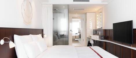Habitación de hotel con una cama grande, un tocador con luces, un televisor y un vestidor.