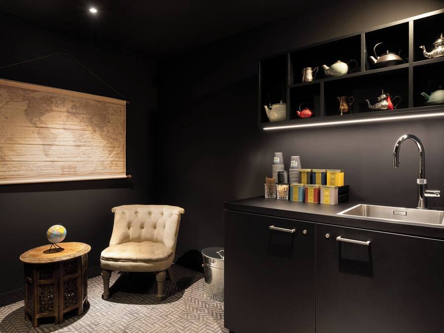 Une cuisine moderne avec des meubles de couleur sombre, une chaise blanche, un globe posé sur une petite table et une carte du monde accrochée au mur.
