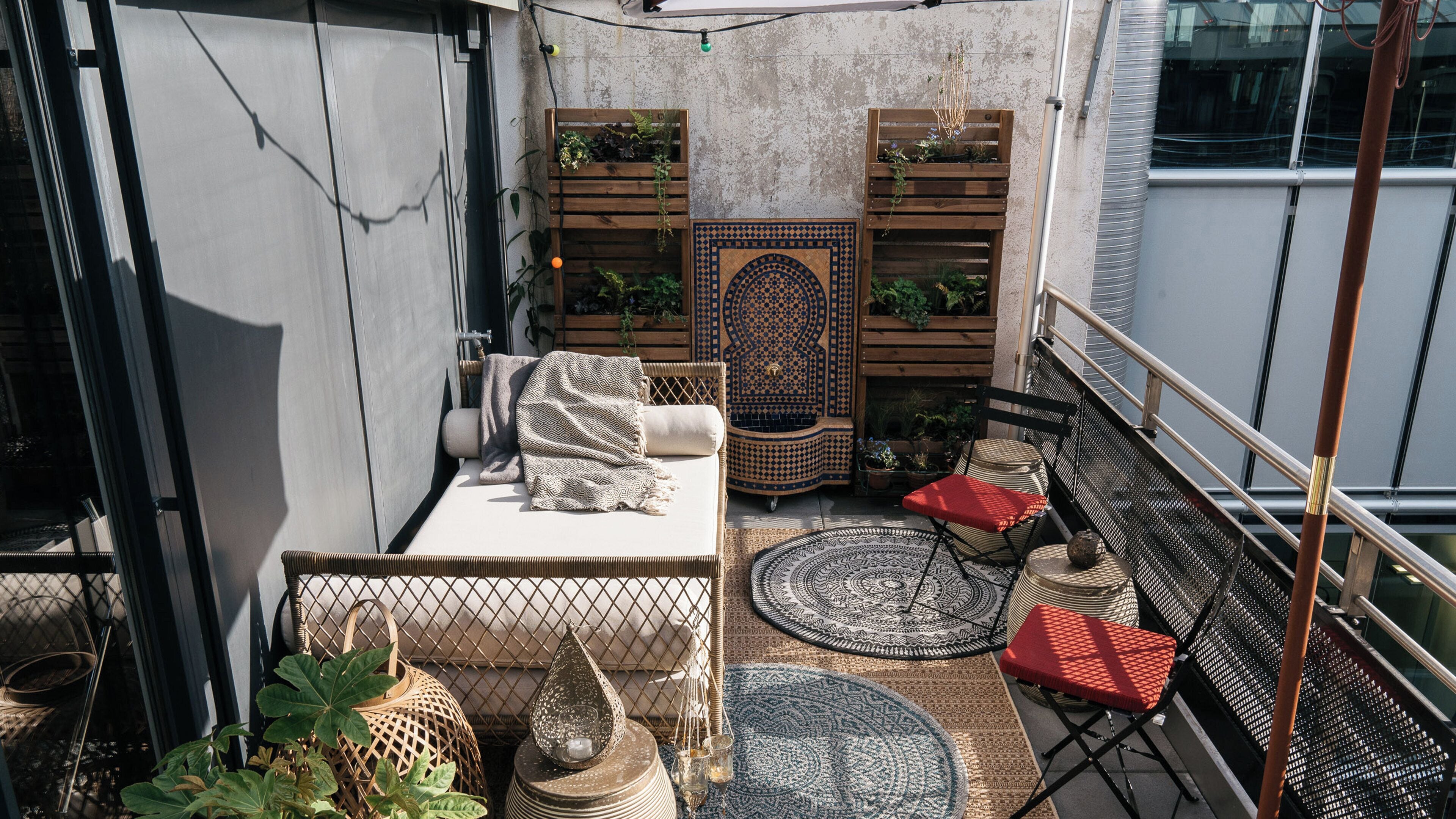 Un pequeño balcón con un sofá, un otomano estampado, una silla y un mueble decorativo con plantas.