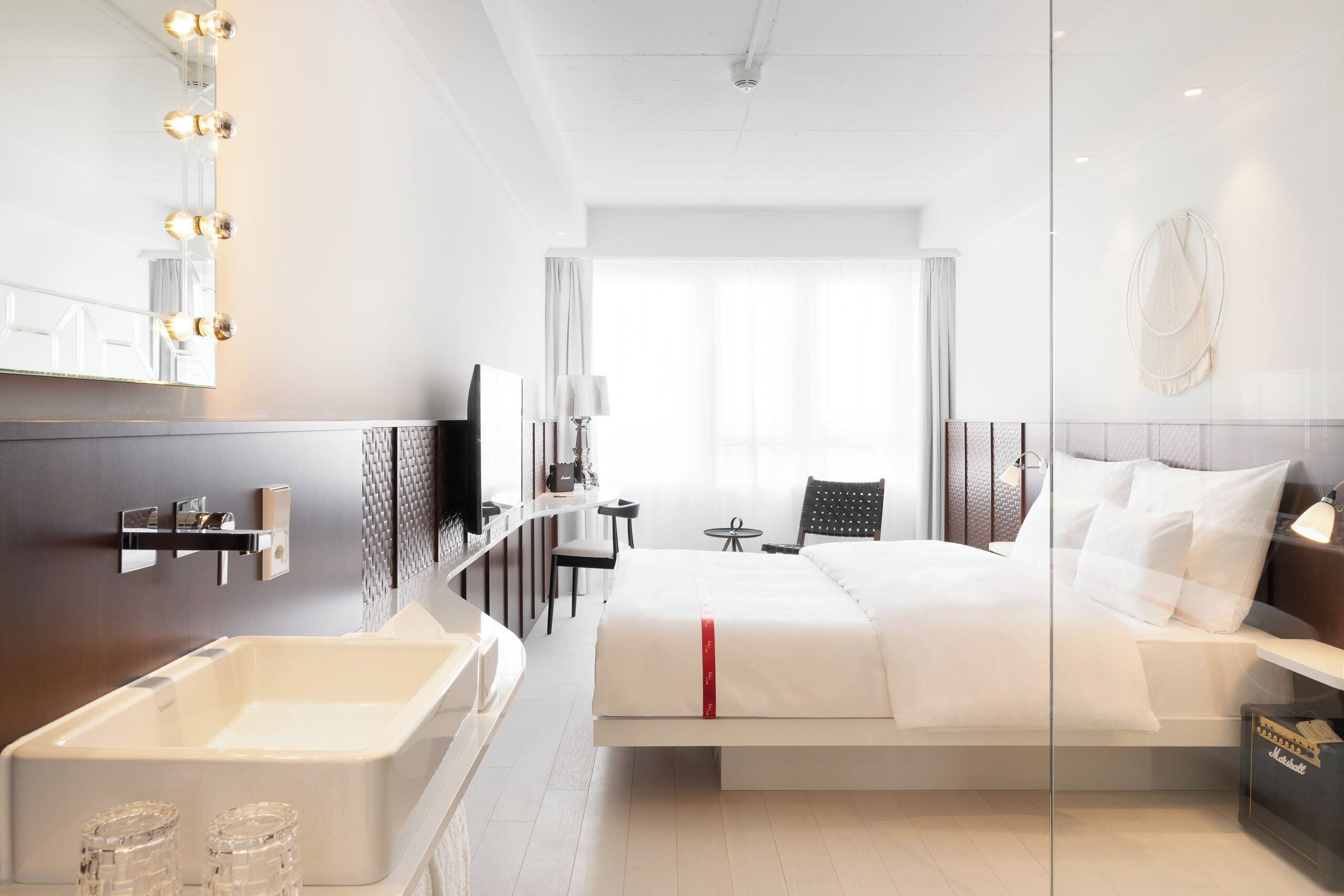 Una habitación de hotel moderna con una cama grande, un baño con bañera, un tocador con espejo y una zona de estar con mesa y sillas.