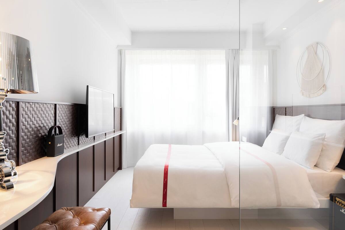 Une chambre d’hôtel moderne équipée d’un lit, d’une télévision, d’un bureau et d’un banc en cuir.