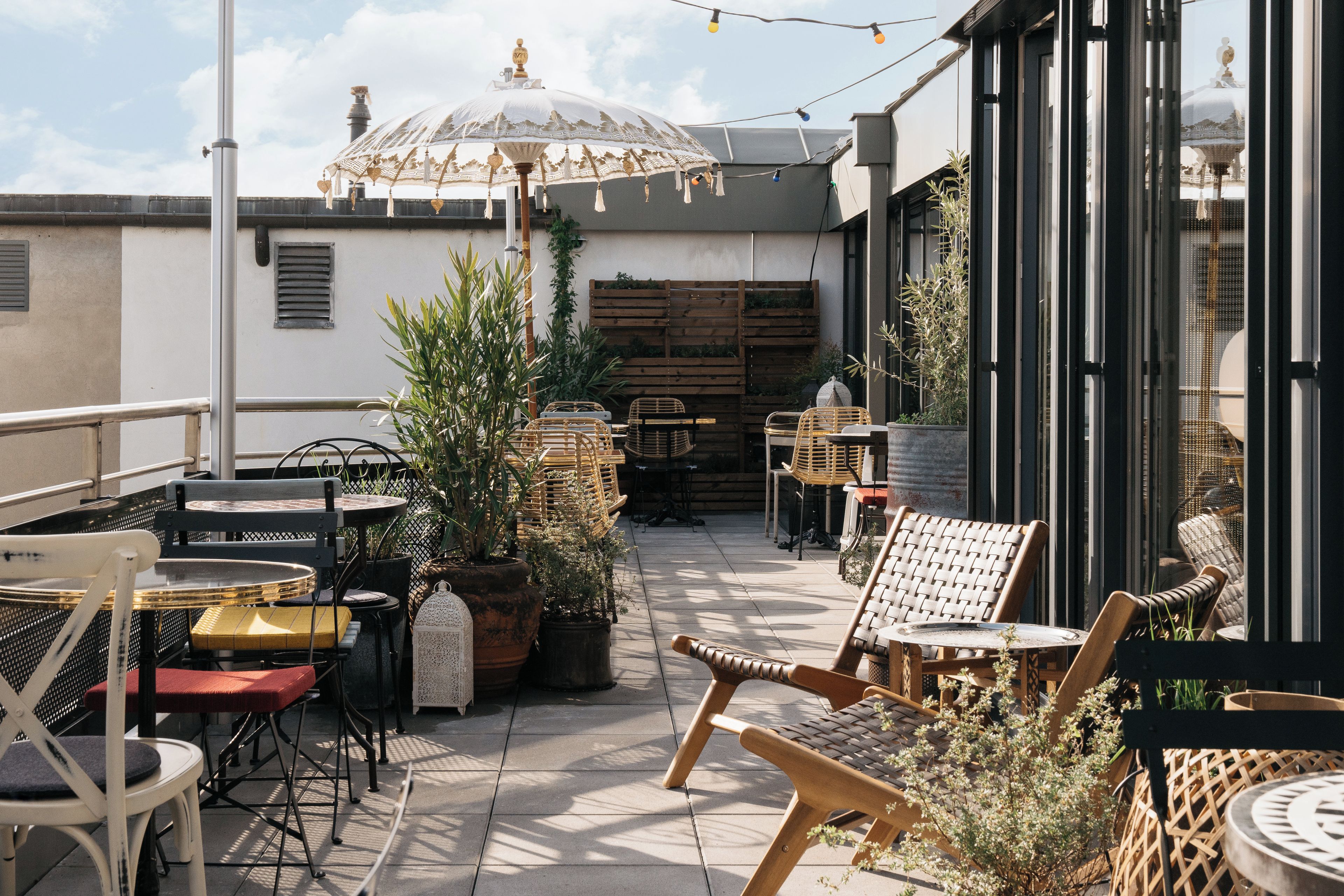 An outdoor seating area with tables and chairs, potted plants, and a decorative umbrella.