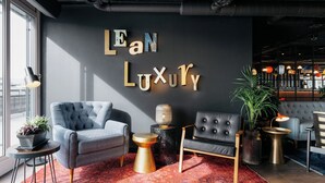 A modern lounge area with a dark wall, two armchairs, a round coffee table, a potted plant, and a red patterned rug. - Ruby Claire Hotel Geneva by IHG (Geneva)