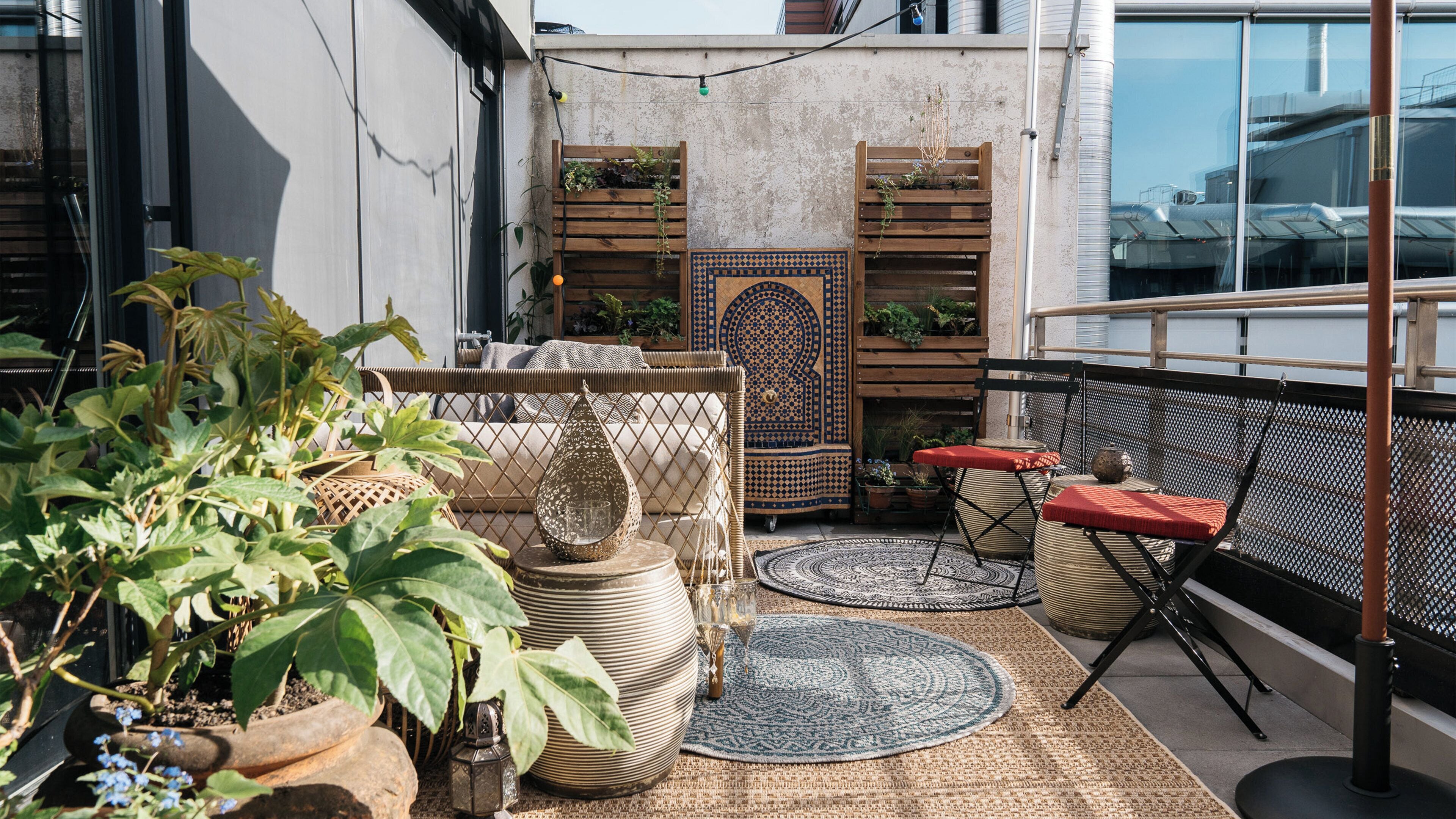 Een balkon met rieten meubilair, een behang met patroon en potplanten.
