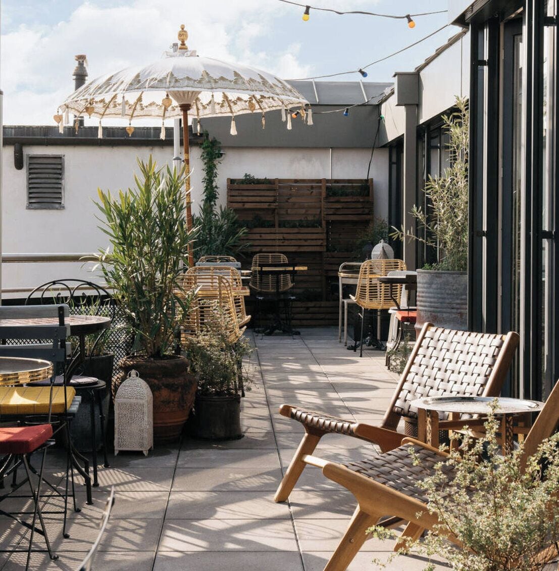 En udendørs terrasse med fletningsmøbler, krukker med planter og en pyntelig parasol.
