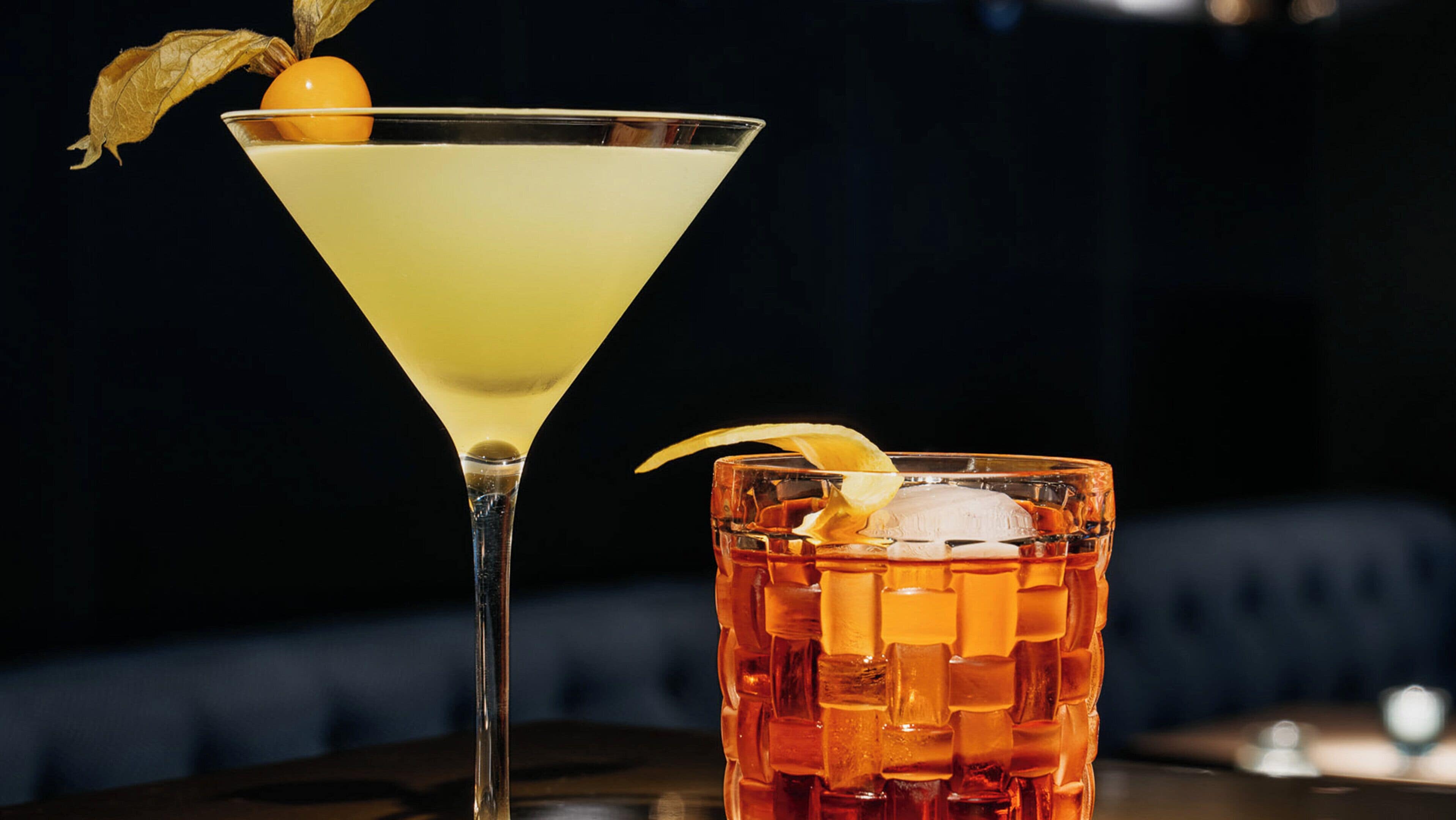A martini glass and a glass with ice cubes and a lemon slice.
