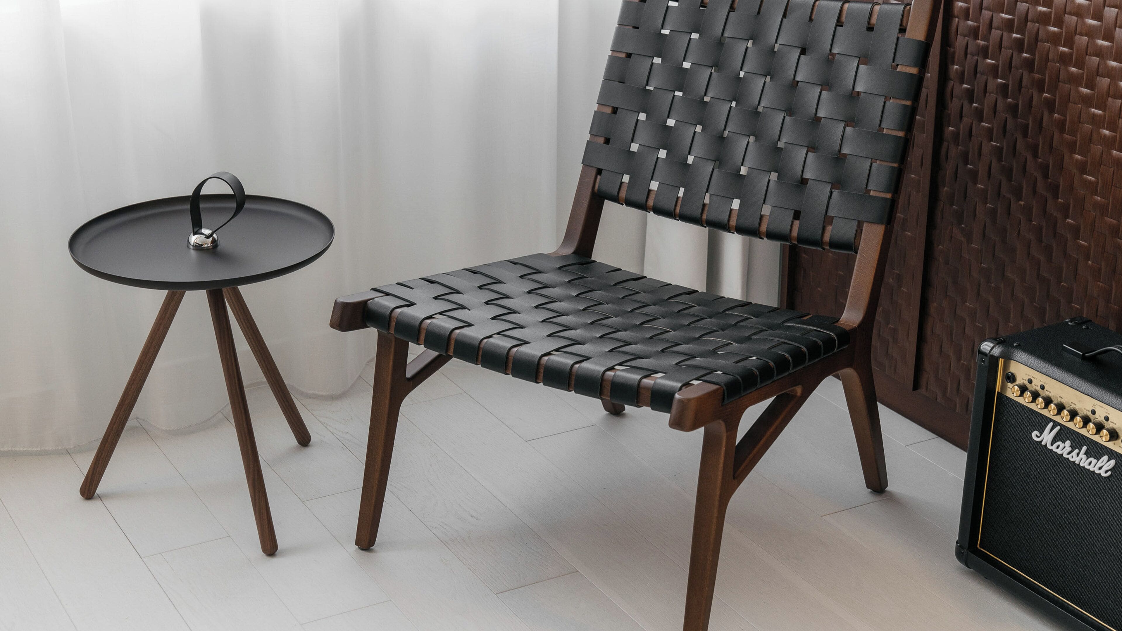 A chair with a woven backrest and seat, a small round table with a metal base, and a Marshall amplifier.