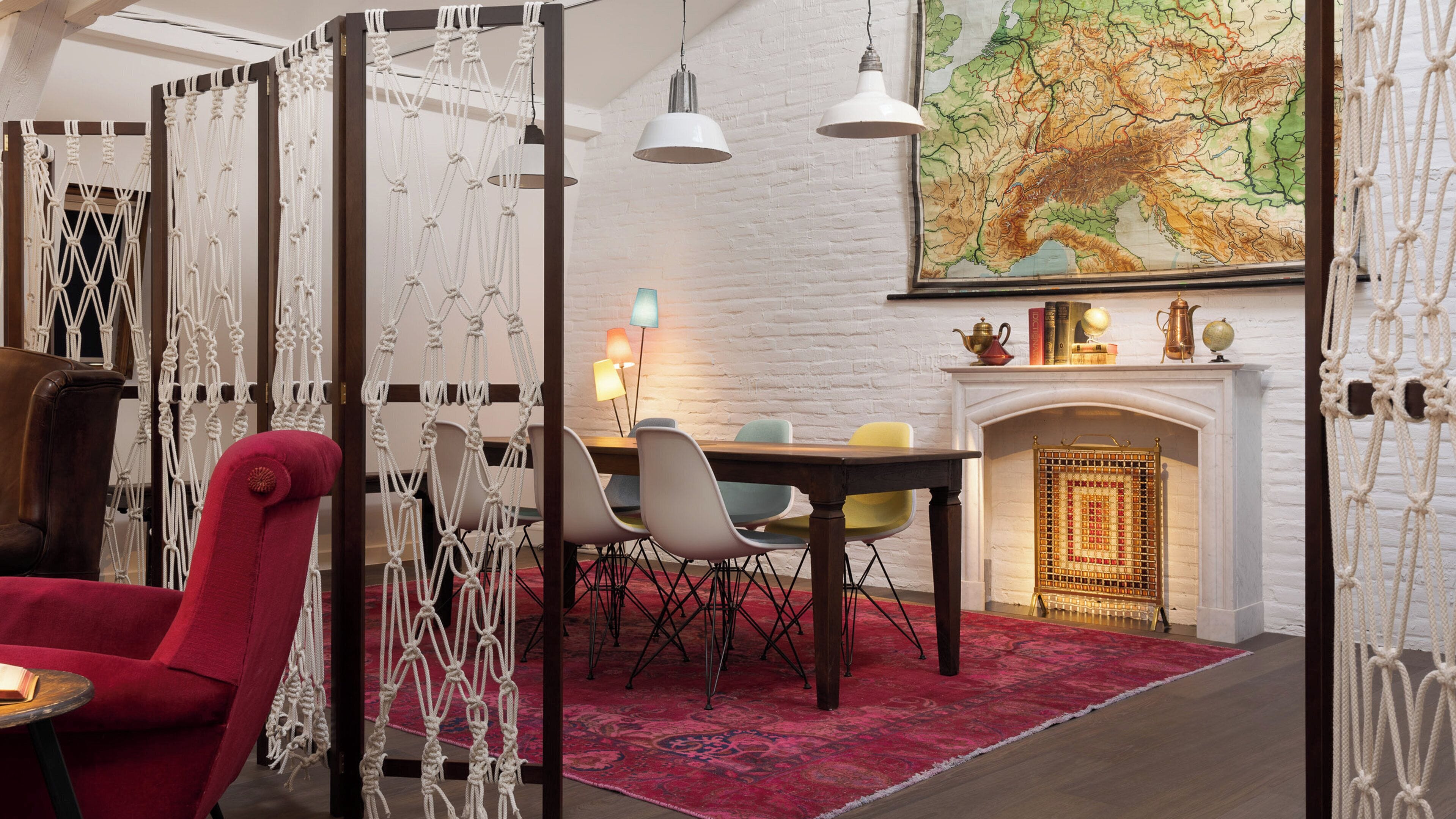 Una habitación con una mesa de comedor, sillas, un sillón rojo, una chimenea y un mapa en la pared.