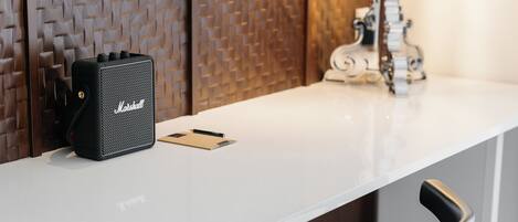Una mesa blanca con un amplificador Marshall negro, un lápiz y un cuaderno.