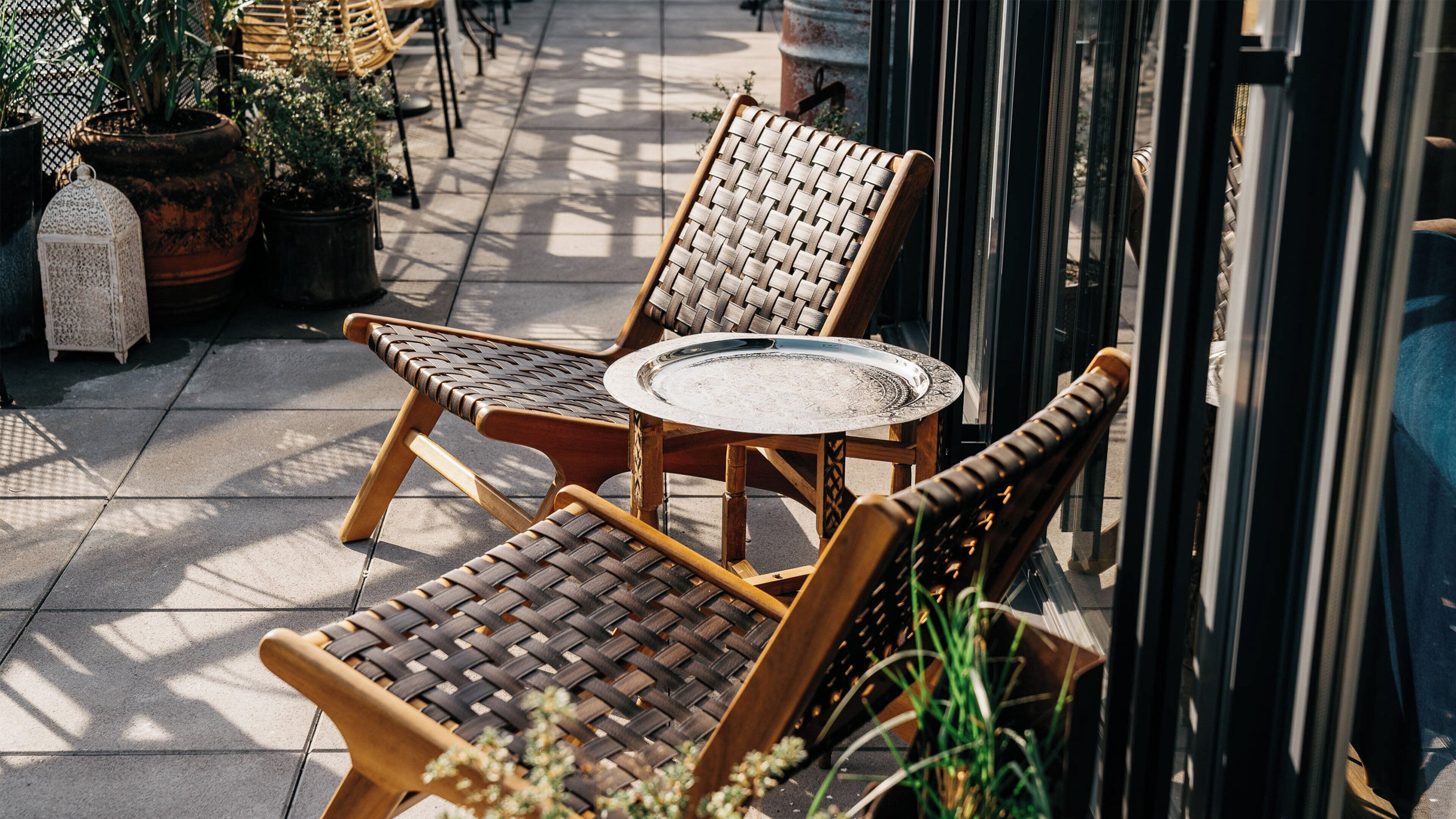 Wicker chairs and a round table outside a building with potted plants and a decorative lantern.