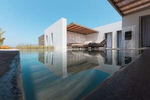 A modern poolside area with a clear view of the pool, a lounge chair, and a covered seating area. - Cove Paros (Paros)