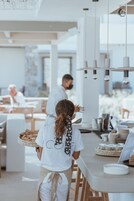 A modern dining area with a long counter, hanging light fixtures, and a person carrying a basket of food.