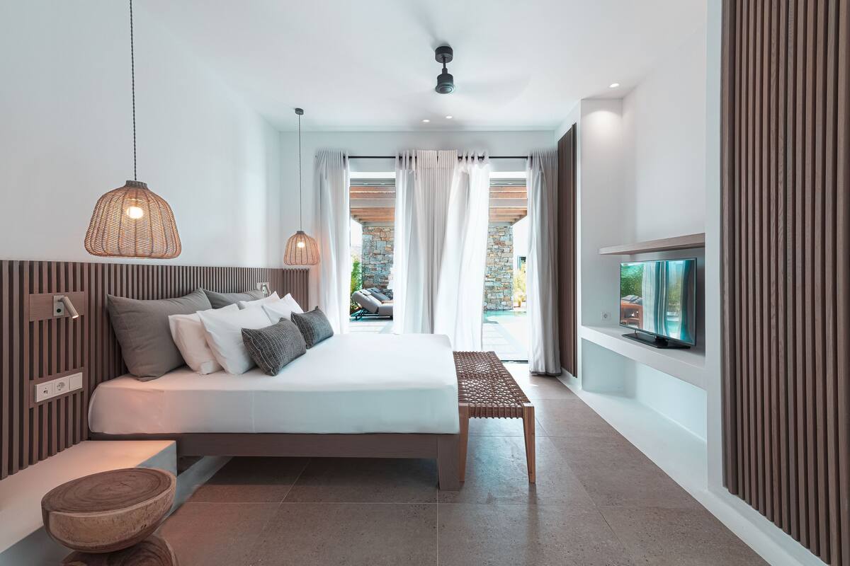 Un dormitorio moderno con cama, mesita de noche, televisor y vistas al exterior.