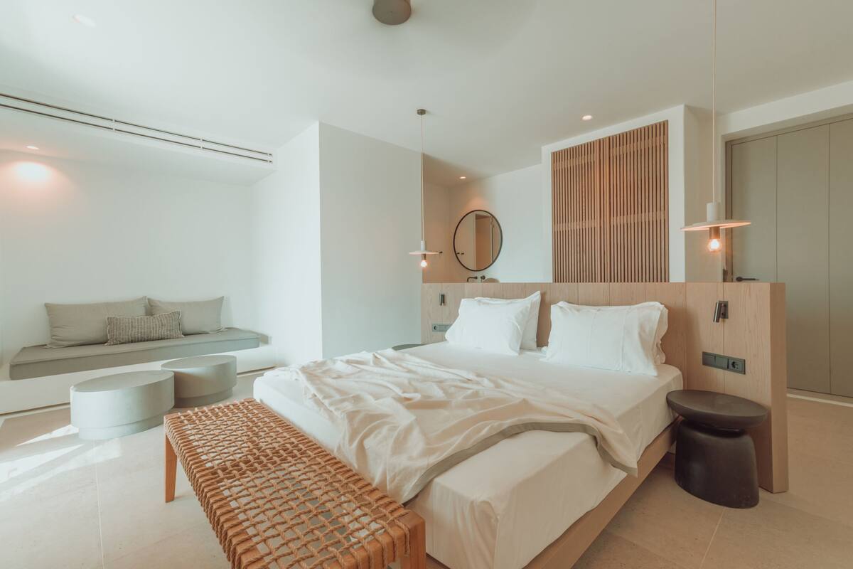 Un dormitorio moderno con una cama grande, un banco, un espejo redondo y un panel de madera empotrado en la pared.