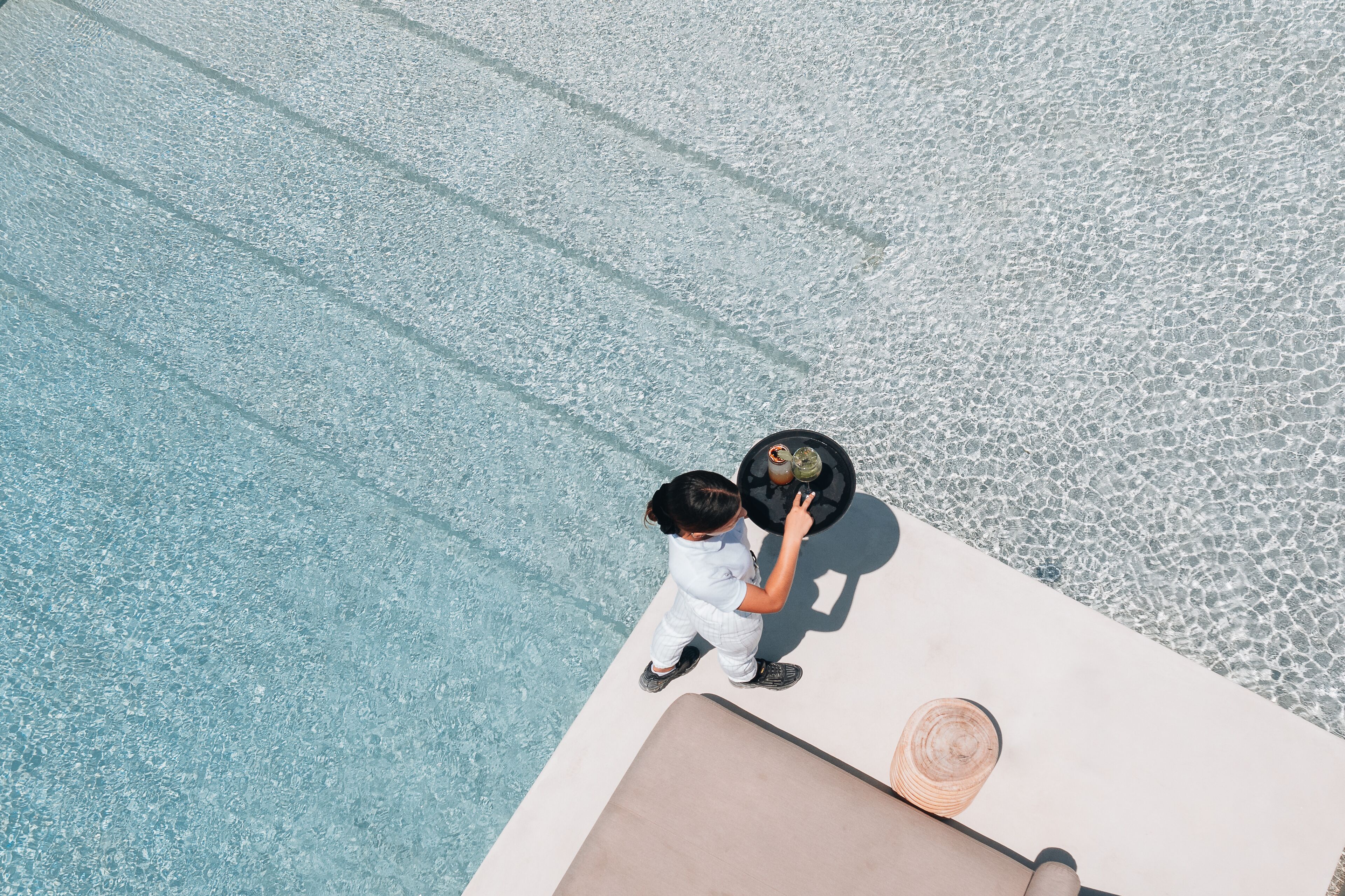 Un enfant se tient près d’une piscine, à côté d’un espace de détente, et un chapeau est posé sur la table.